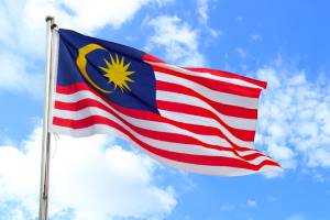 Fahne von Malaysia vor blauem Himmel mit kleinen Wolken