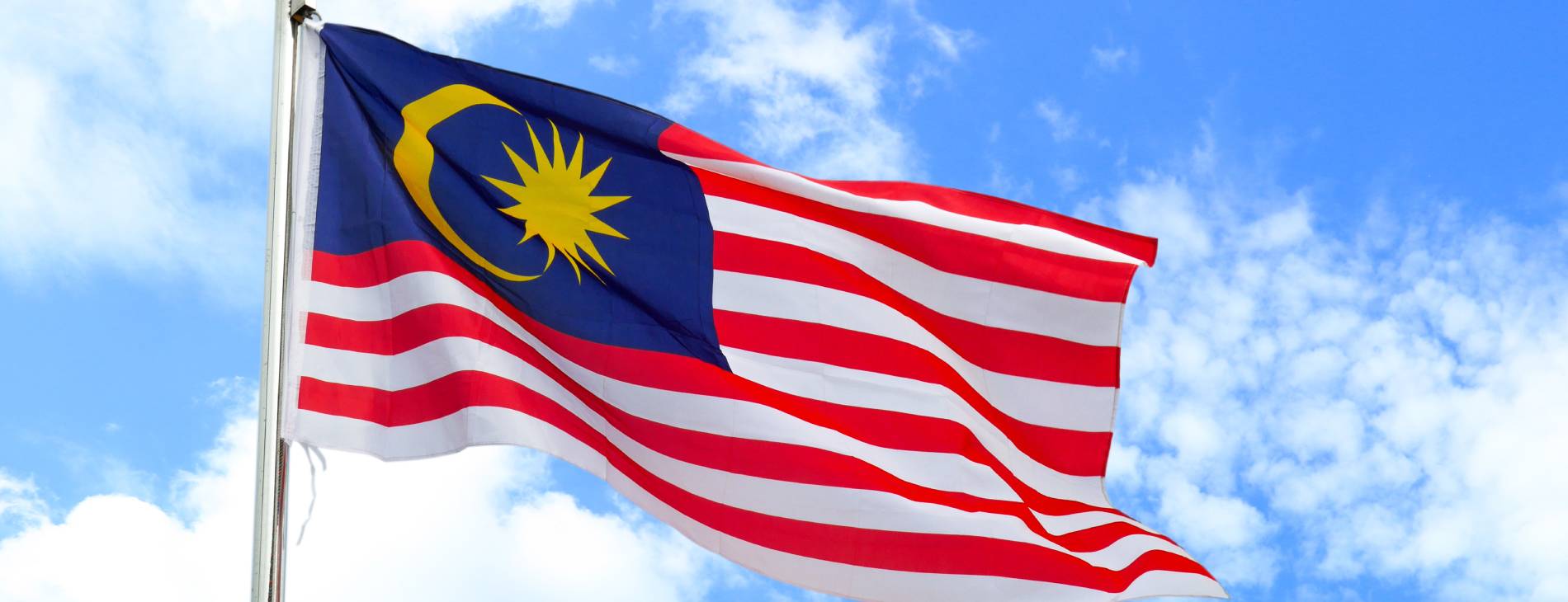 Fahne von Malaysia vor blauem Himmel mit kleinen Wolken